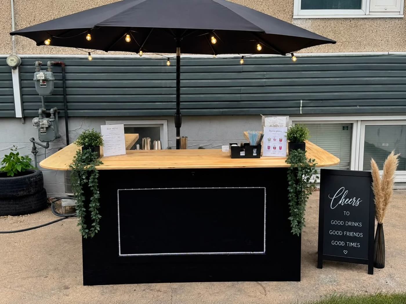 Black pop-up bar with "Cheers" sign, greenery, and pampas grass